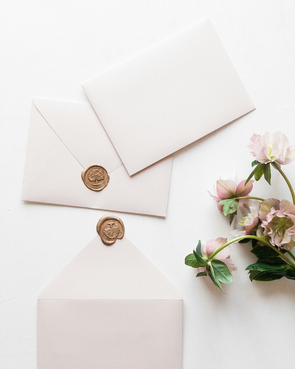 Cream envelopes with gold wax seals beside pink flowers